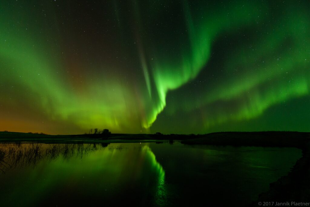 Green northern lights reflected on still water